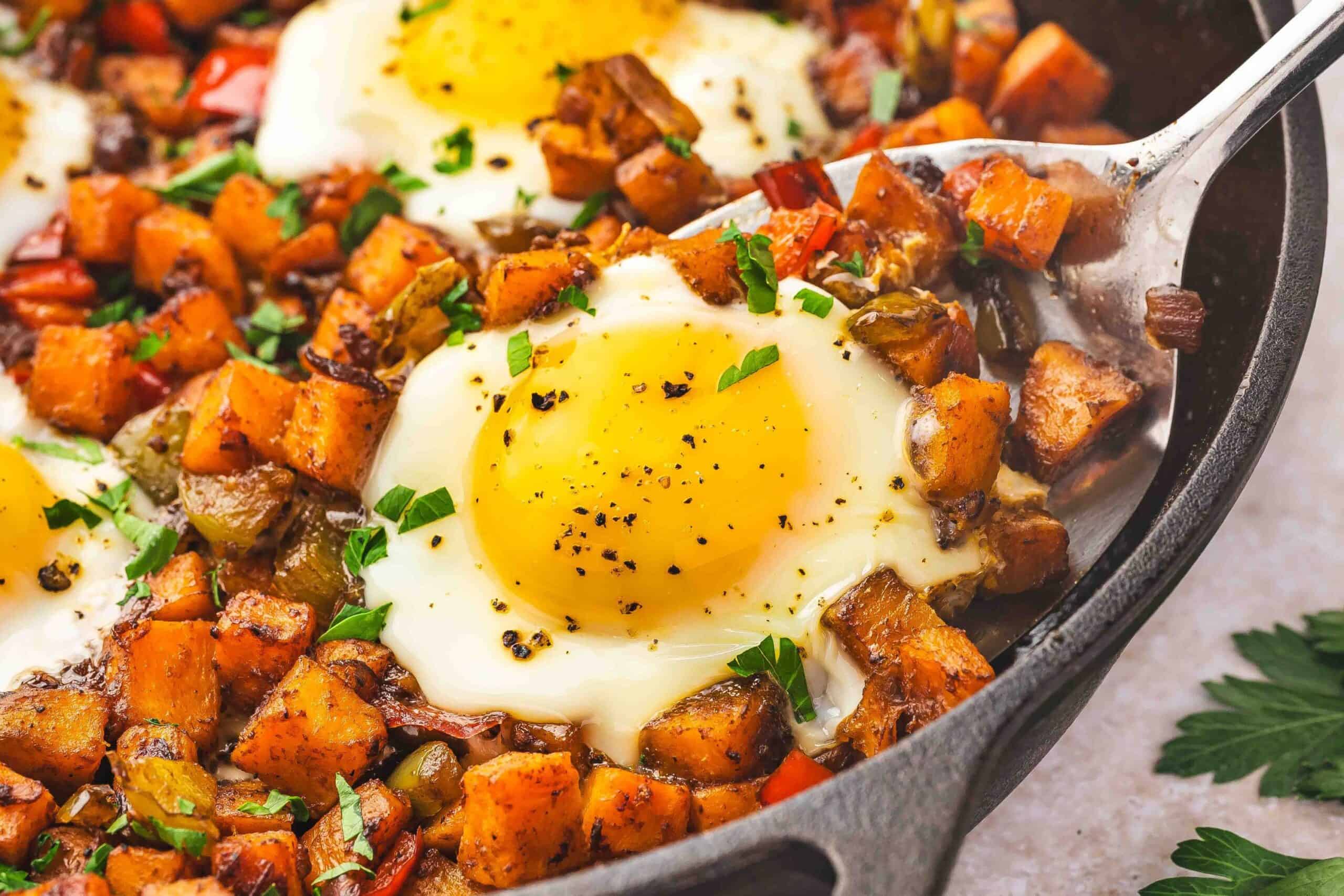 Close-up of a spatula scooping sweet potato hash with a runny egg from a cast iron skillet