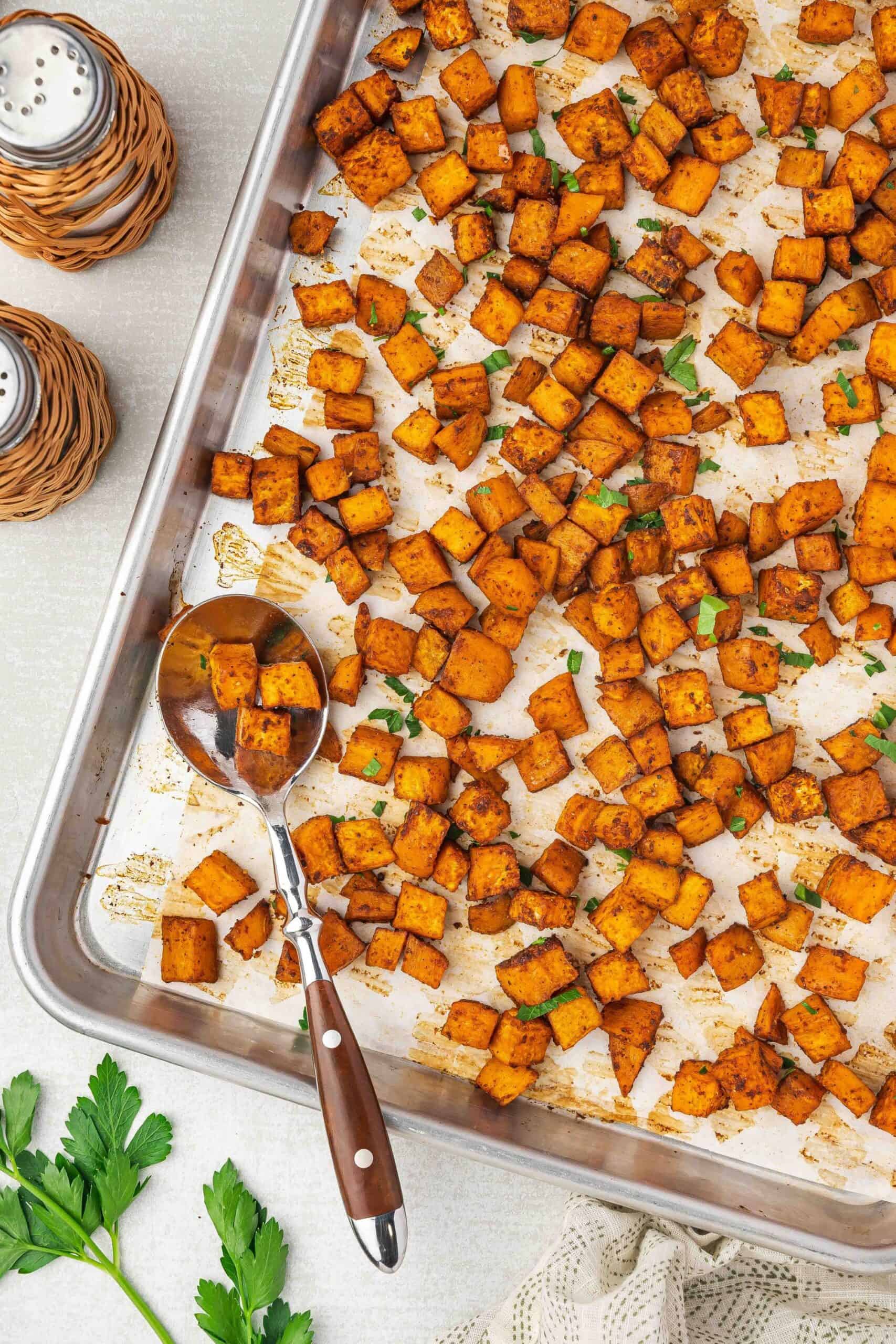 Golden crispy roasted sweet potato cubes spread evenly on a parchment-lined baking sheet.