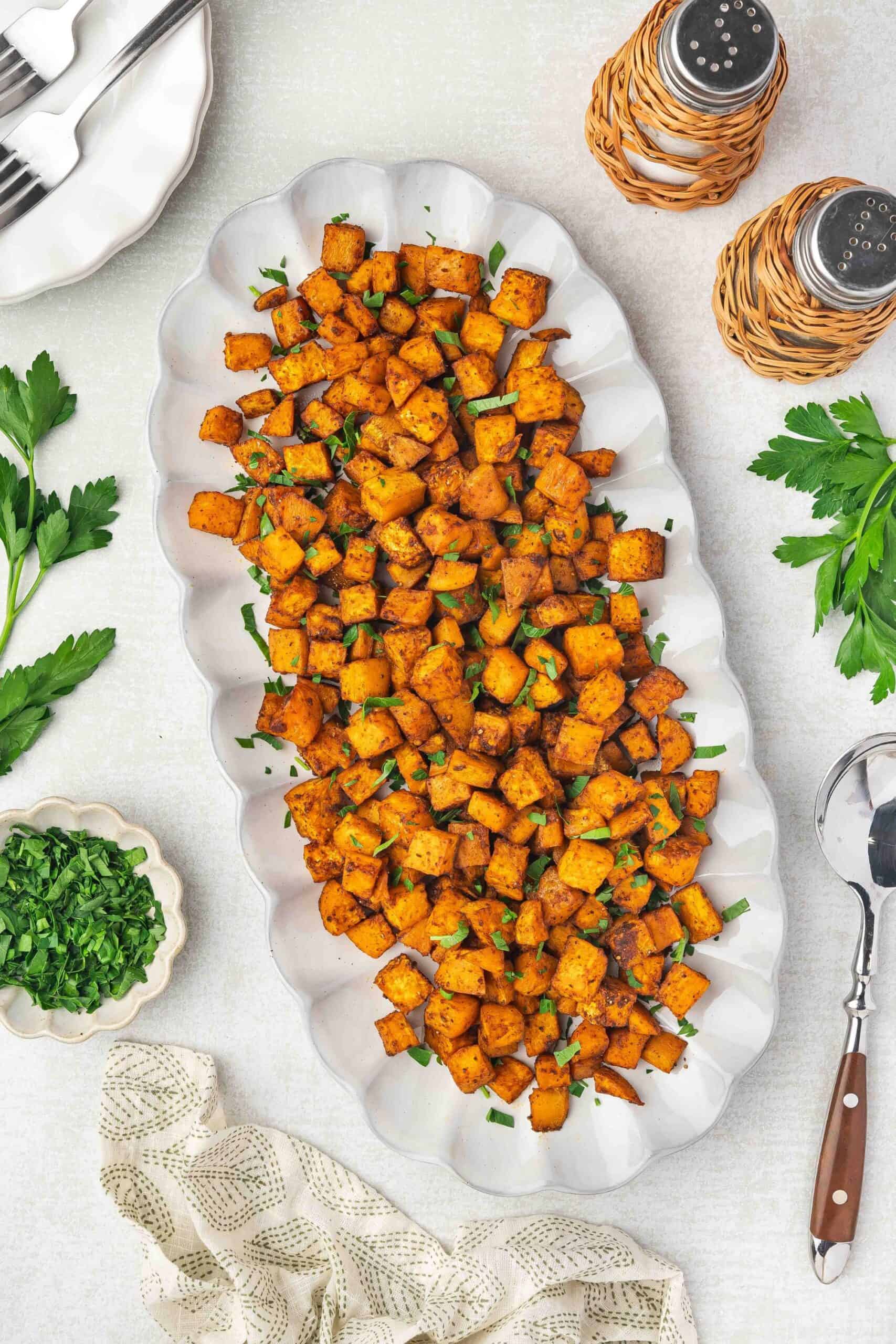 Golden crispy roasted sweet potatoes served on a white ceramic platter garnished with fresh parsley.
