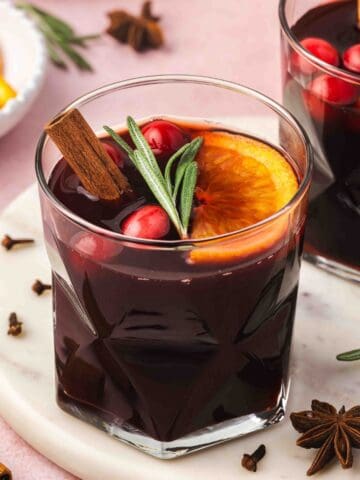 Slow cooker mulled wine poured into mugs, topped with rosemary sprigs and orange slices for a festive look.