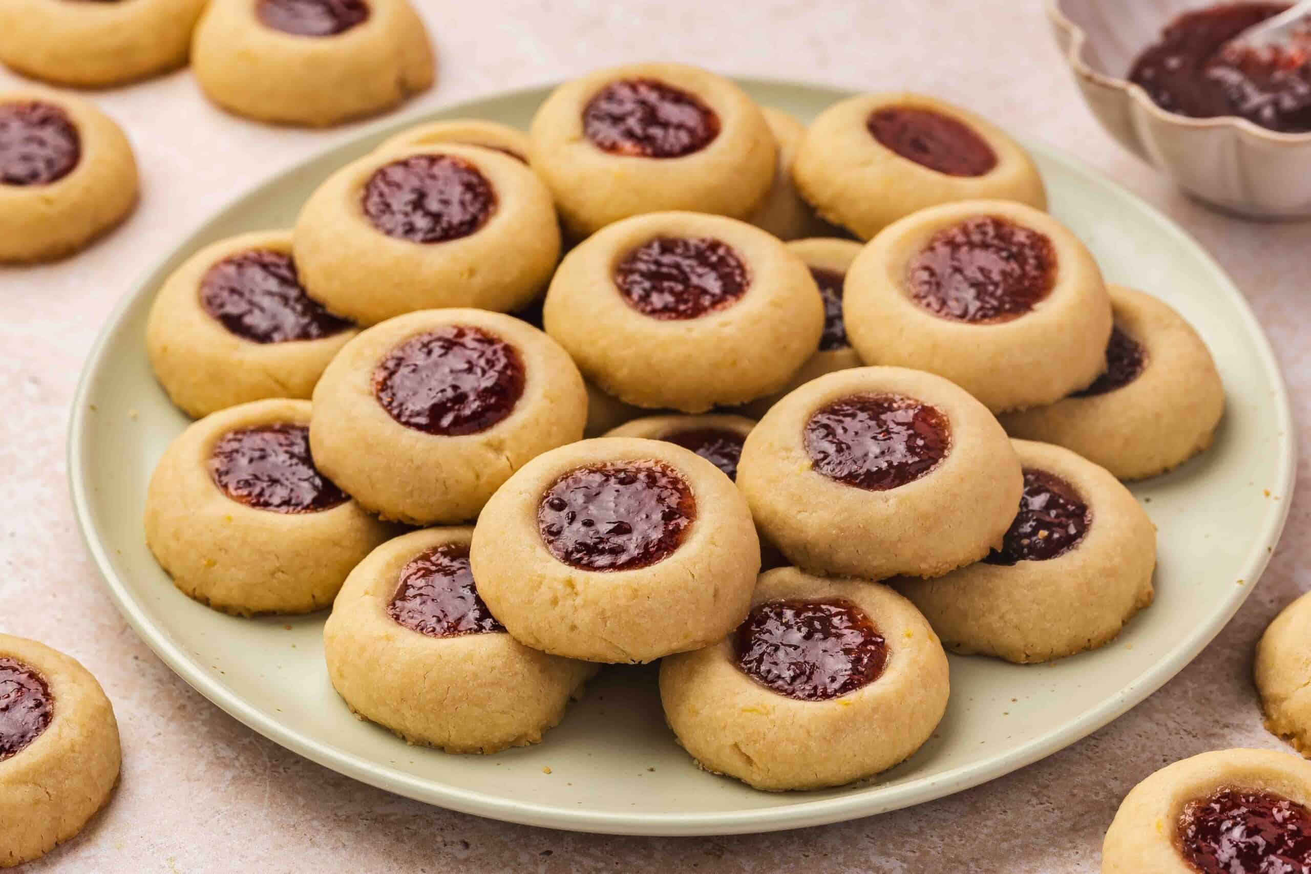 Raspberry thumbprint cookies and a small bowl of raspberry jam styled for a cozy afternoon treat.