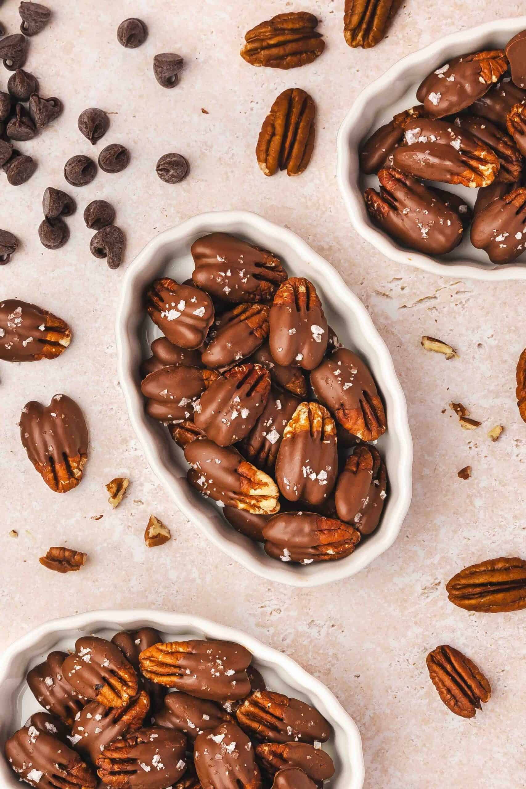 Chocolate-covered pecans in a ceramic snack bowl with flaky sea salt on top.