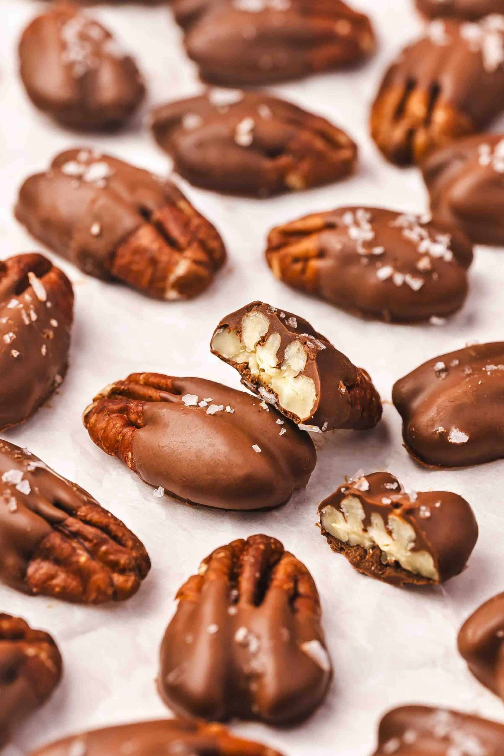 Chocolate-dipped pecans with uneven rustic chocolate coverage on parchment paper for a natural look.