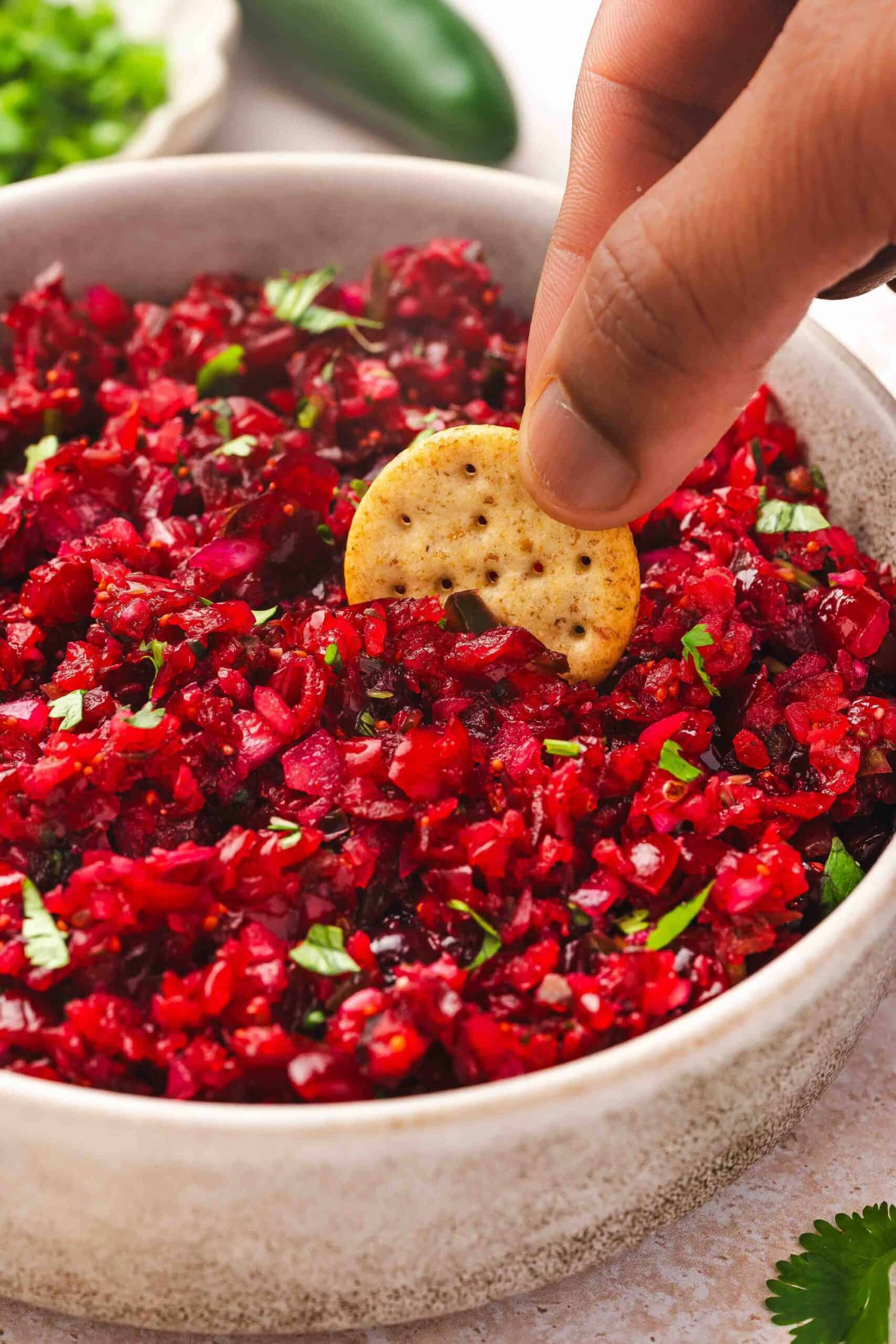Hand scooping cranberry jalapeño salsa with a multigrain cracker