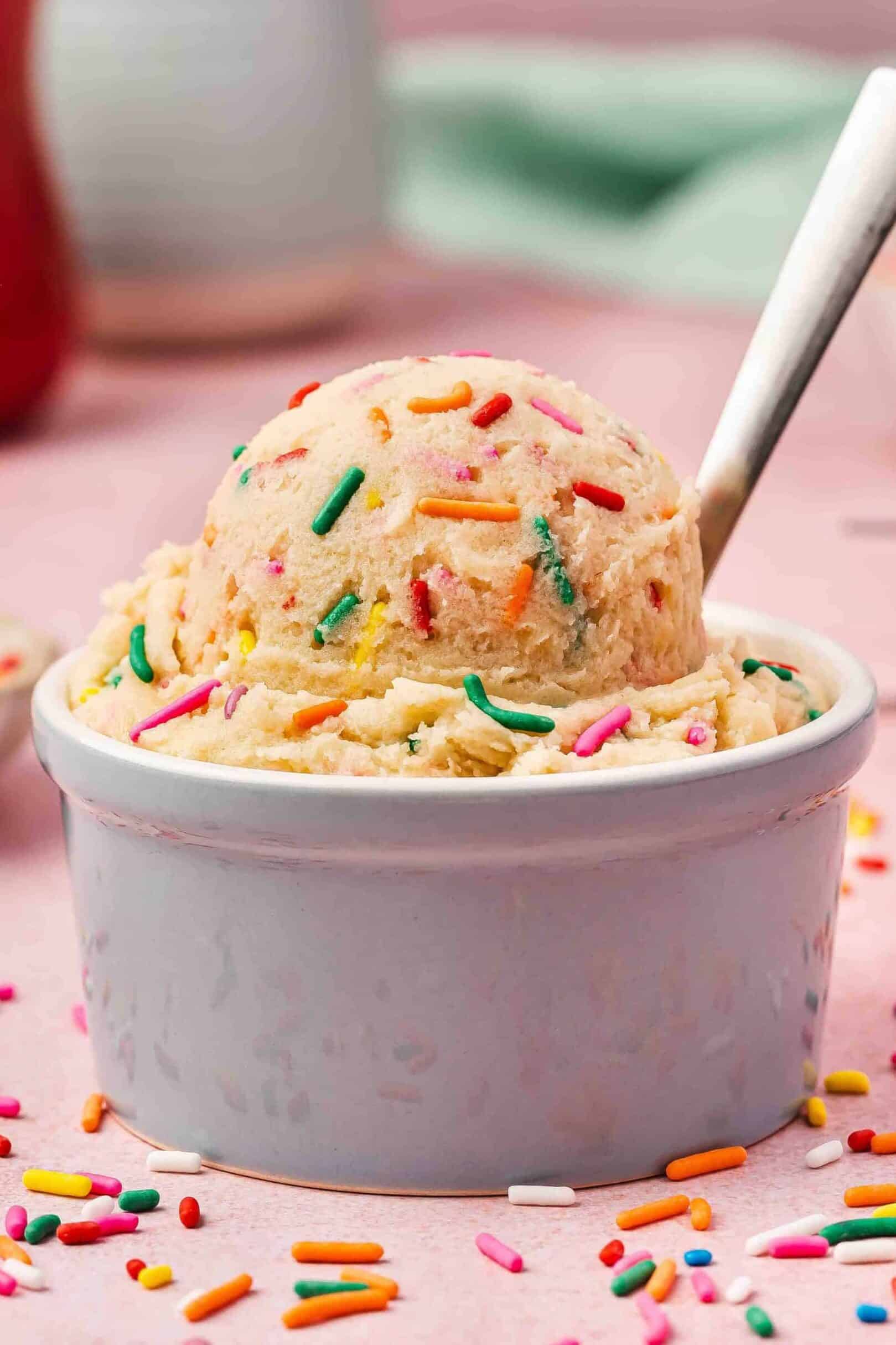 Creamy edible sugar cookie dough in a ceramic bowl with colorful sprinkles on top.