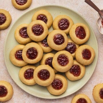 Raspberry thumbprint cookies arranged in neat rows on parchment paper, showing golden edges and bright jam centers.