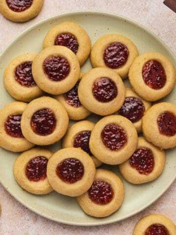 Raspberry thumbprint cookies arranged in neat rows on parchment paper, showing golden edges and bright jam centers.