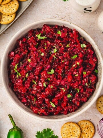 Fresh cranberry jalapeño salsa served in a white ceramic bowl with multigrain crackers