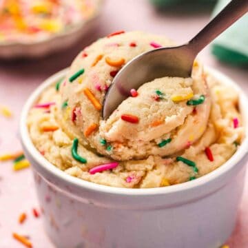 Creamy edible sugar cookie dough in a ceramic bowl with colorful sprinkles on top, ready to eat.