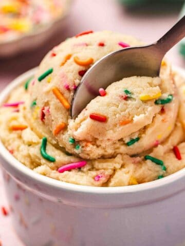 Creamy edible sugar cookie dough in a ceramic bowl with colorful sprinkles on top, ready to eat.