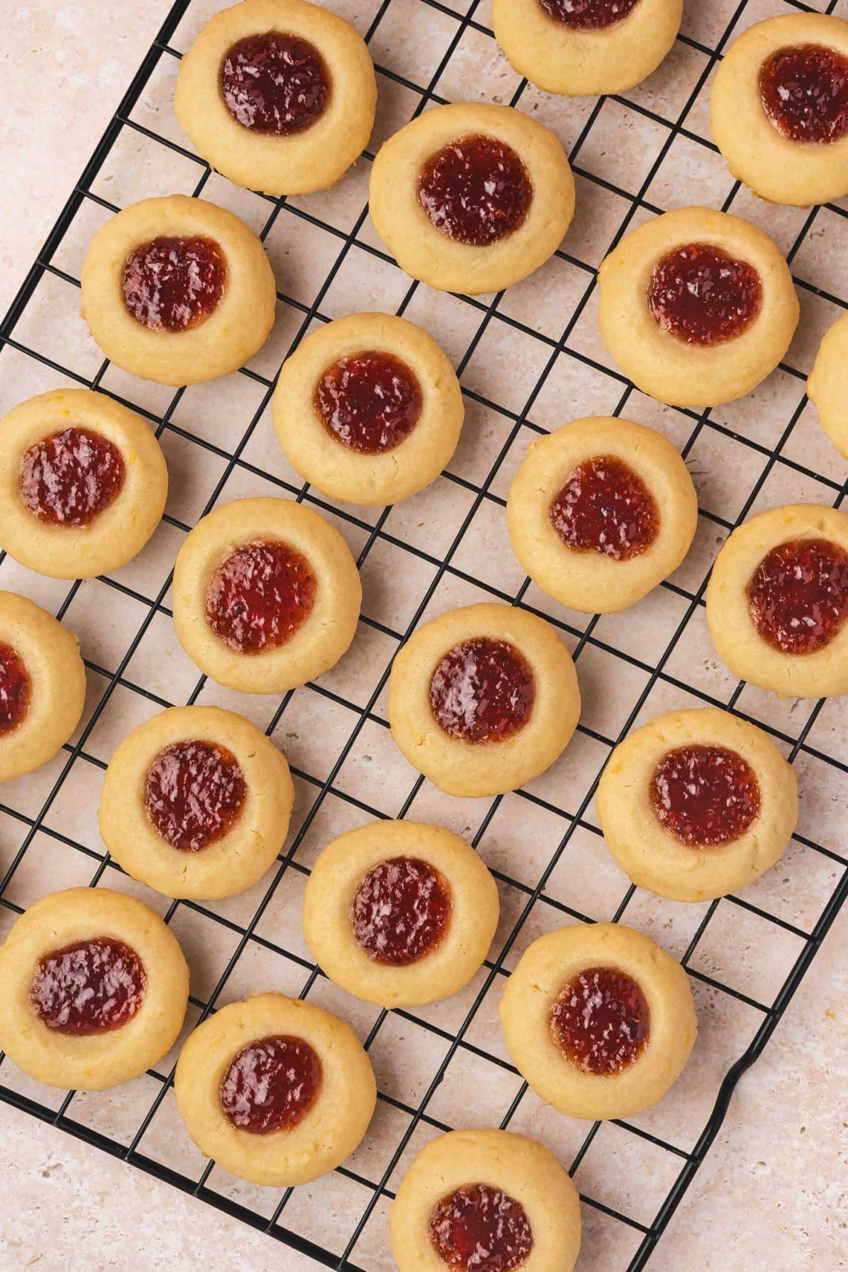 Raspberry thumbprint cookies cooling on a wire rack, showcasing lightly golden edges and glistening jam.