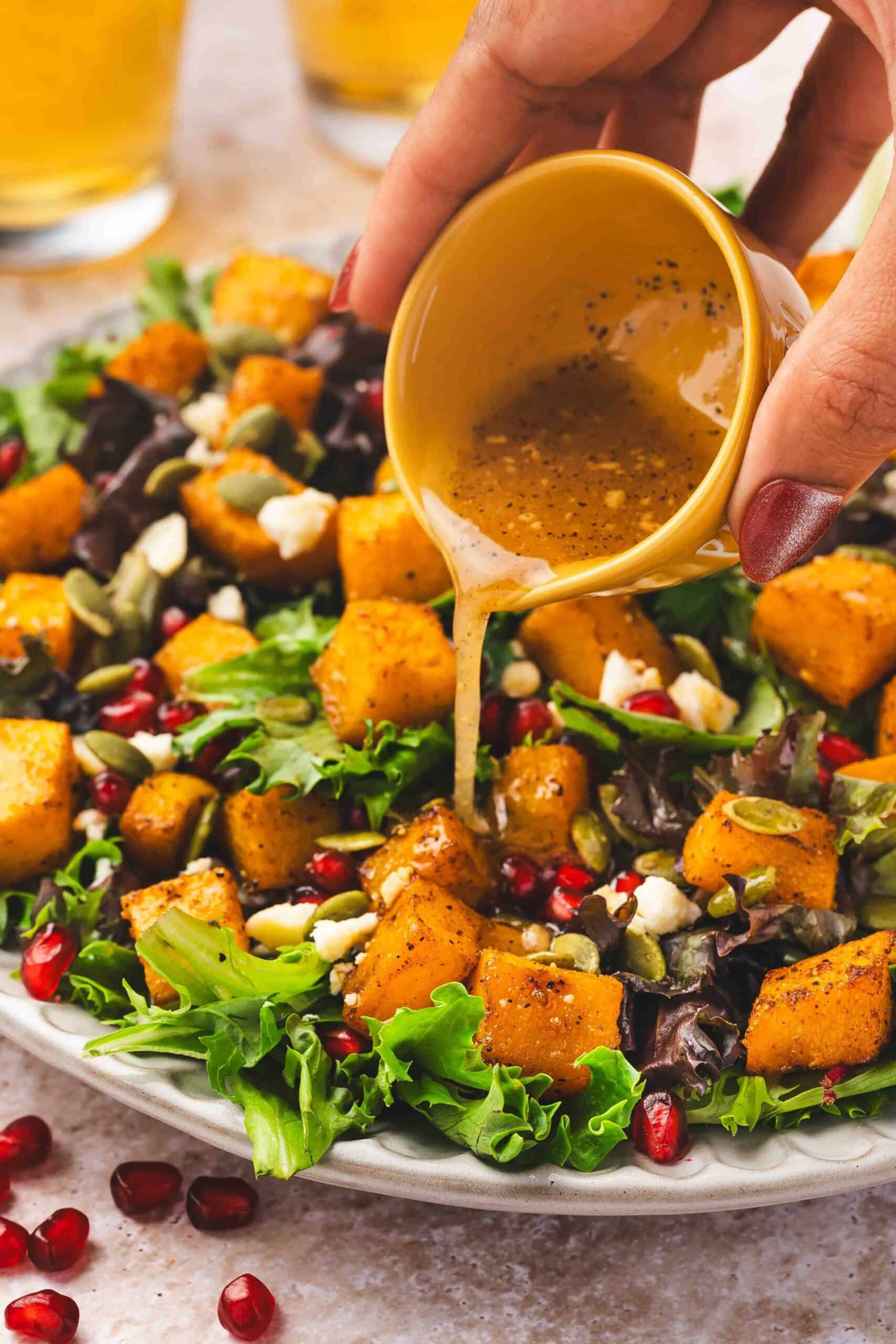 Close-up of dressing being poured over a festive roasted squash and feta salad