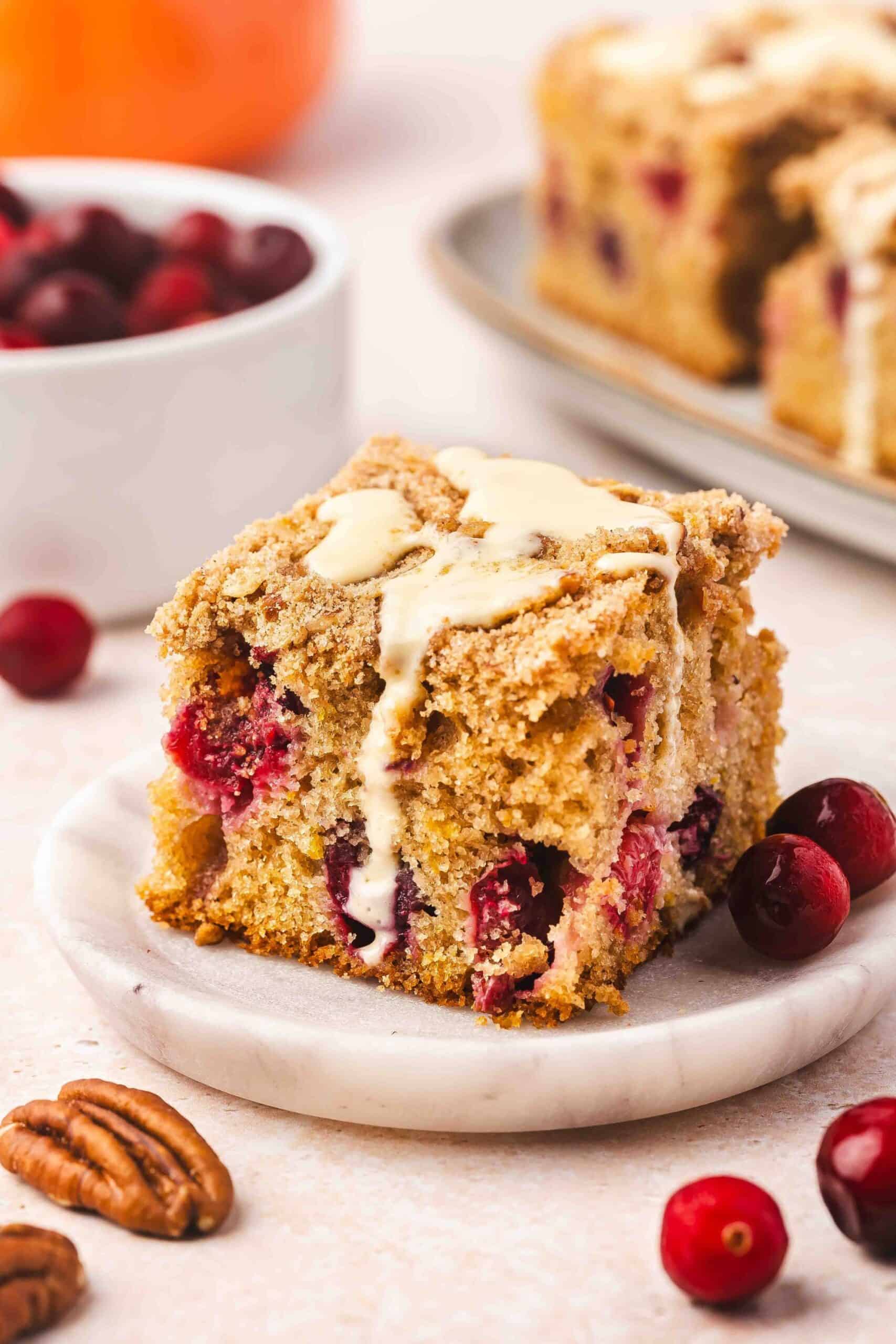 Slice of cranberry orange coffee cake on a white plate with orange slices on the side