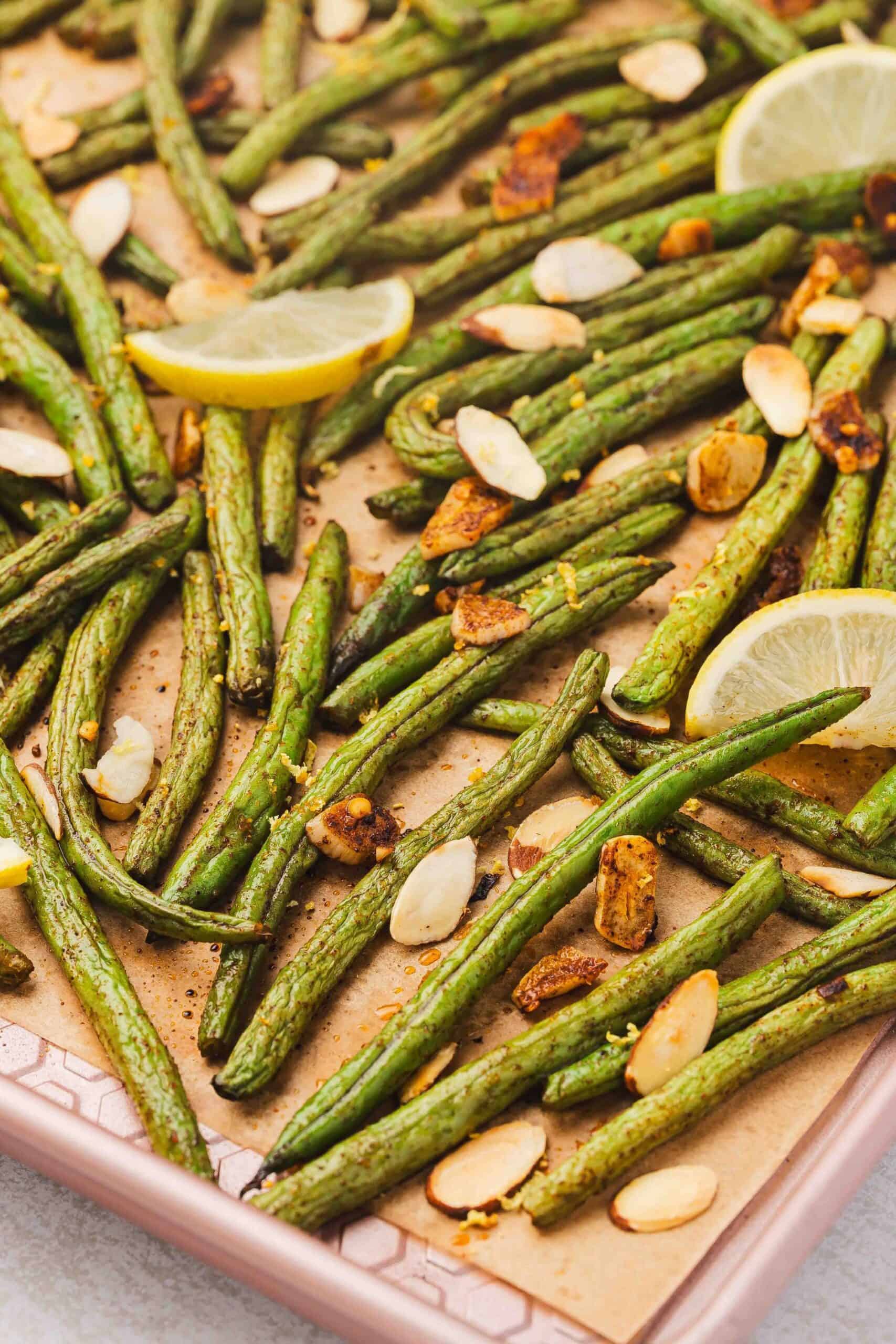 Flatlay of roasted green beans with lemon slices and toasted almonds.