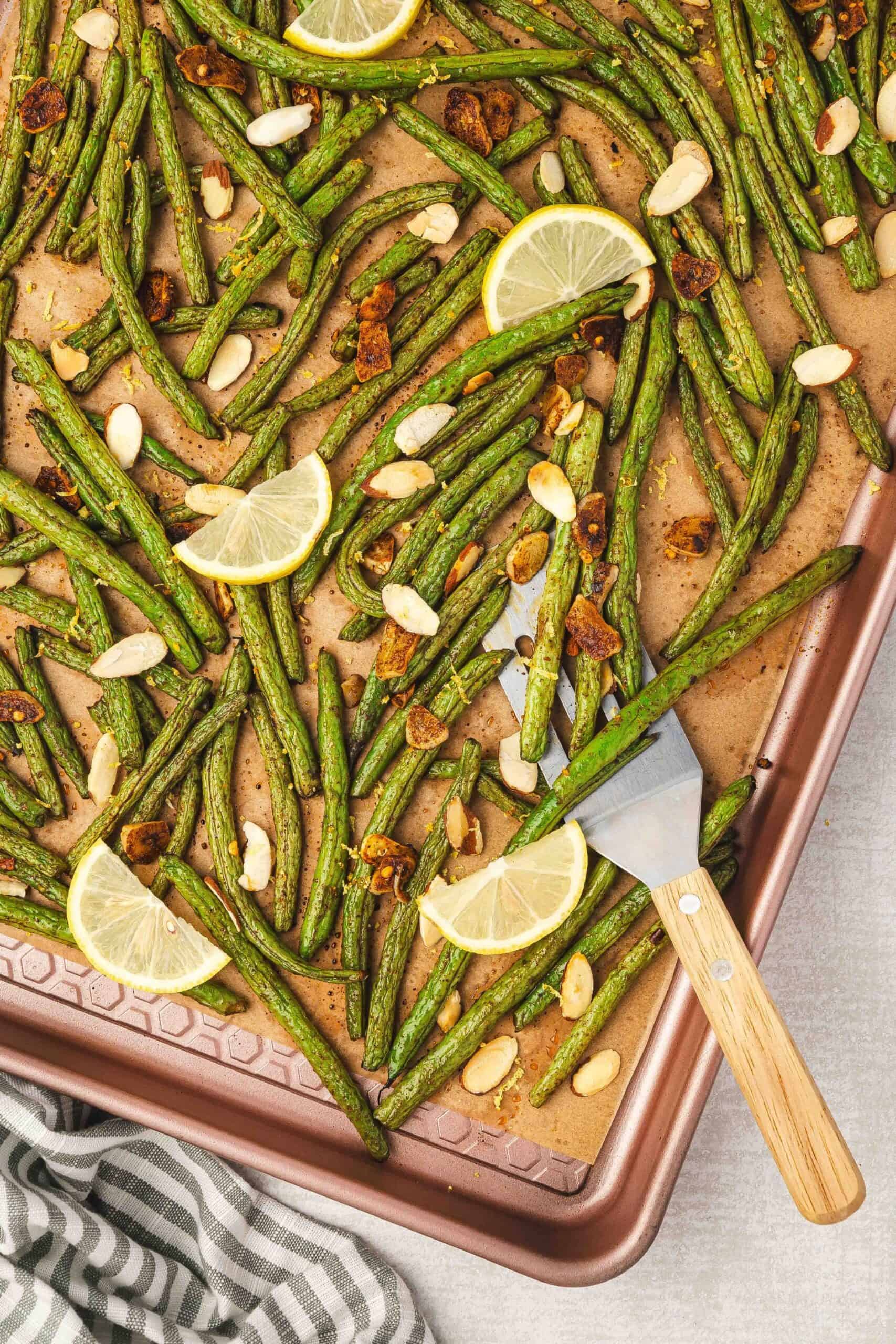 Crispy roasted green beans topped with almonds and lemon wedges for serving.