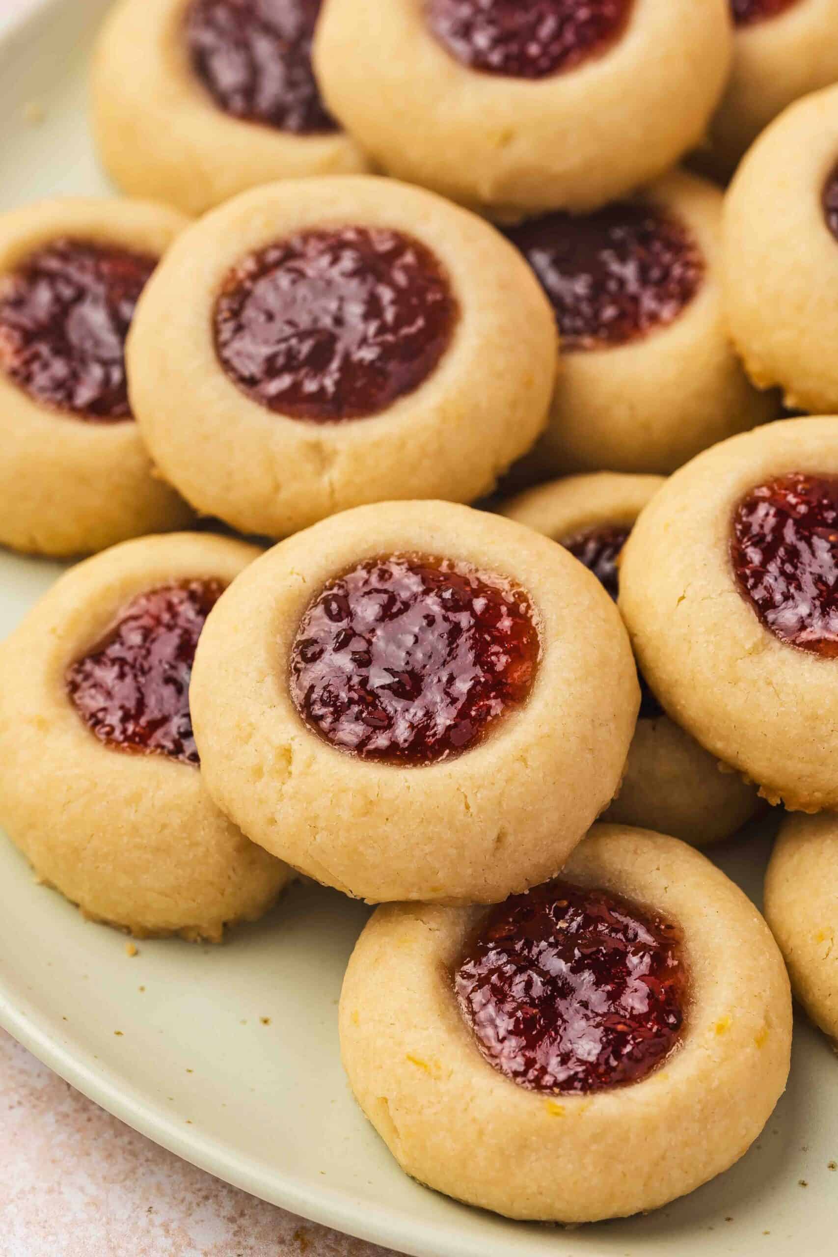 Thumbprint cookie in focus with visible buttery texture and glossy jam pool in the center.