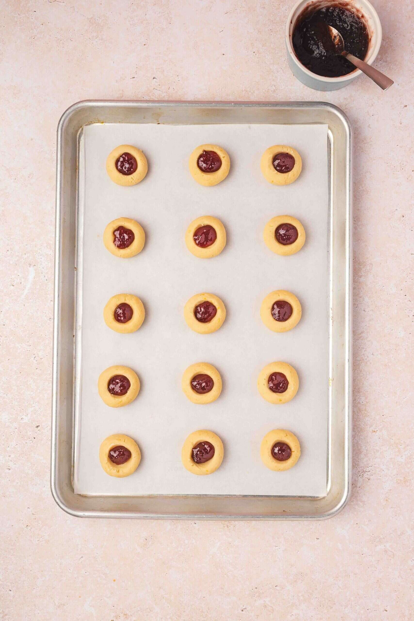 Filling chilled thumbprint cookies with raspberry jam before baking in the oven.