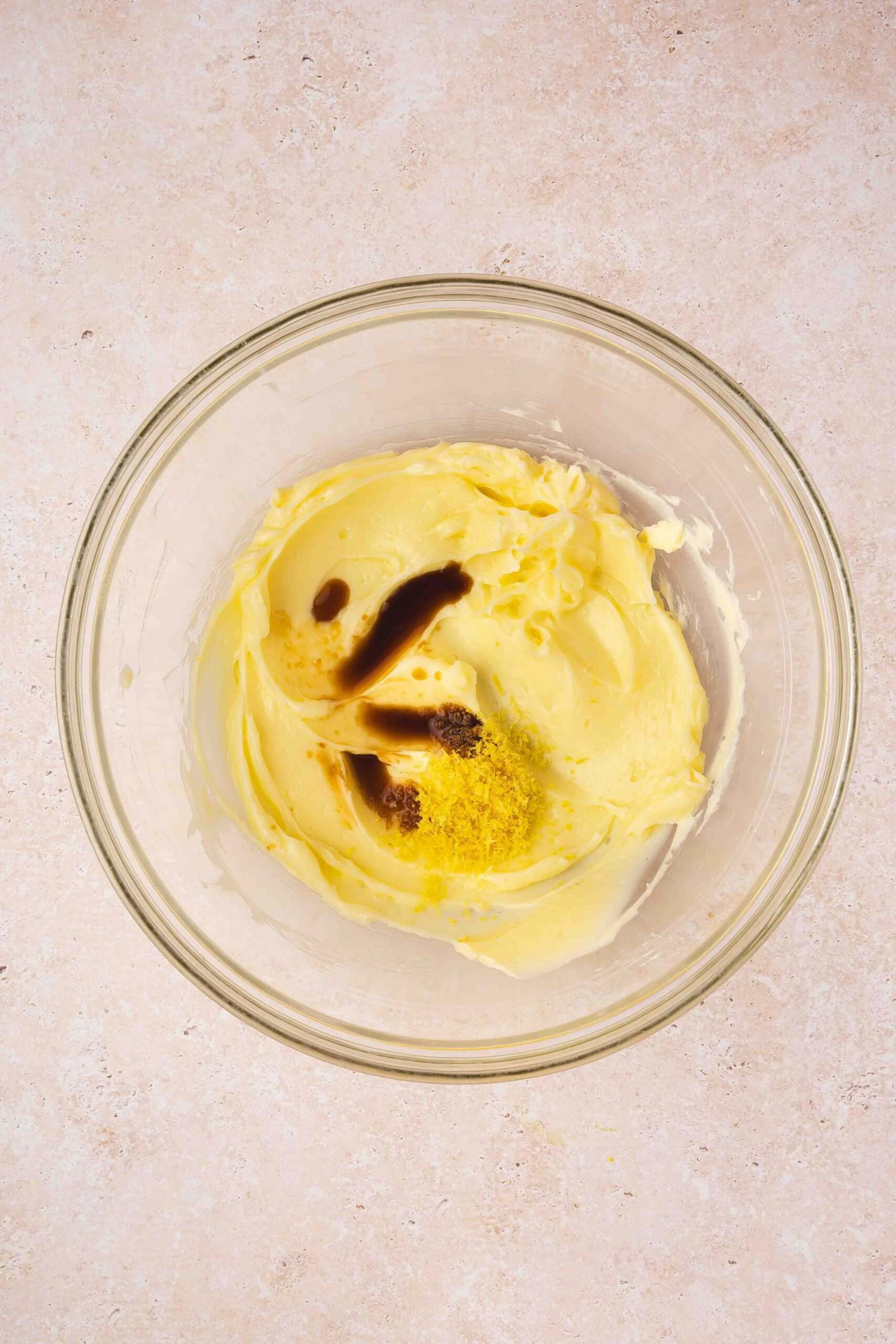 Vanilla extract and fresh lemon zest being added to the creamy butter mixture.