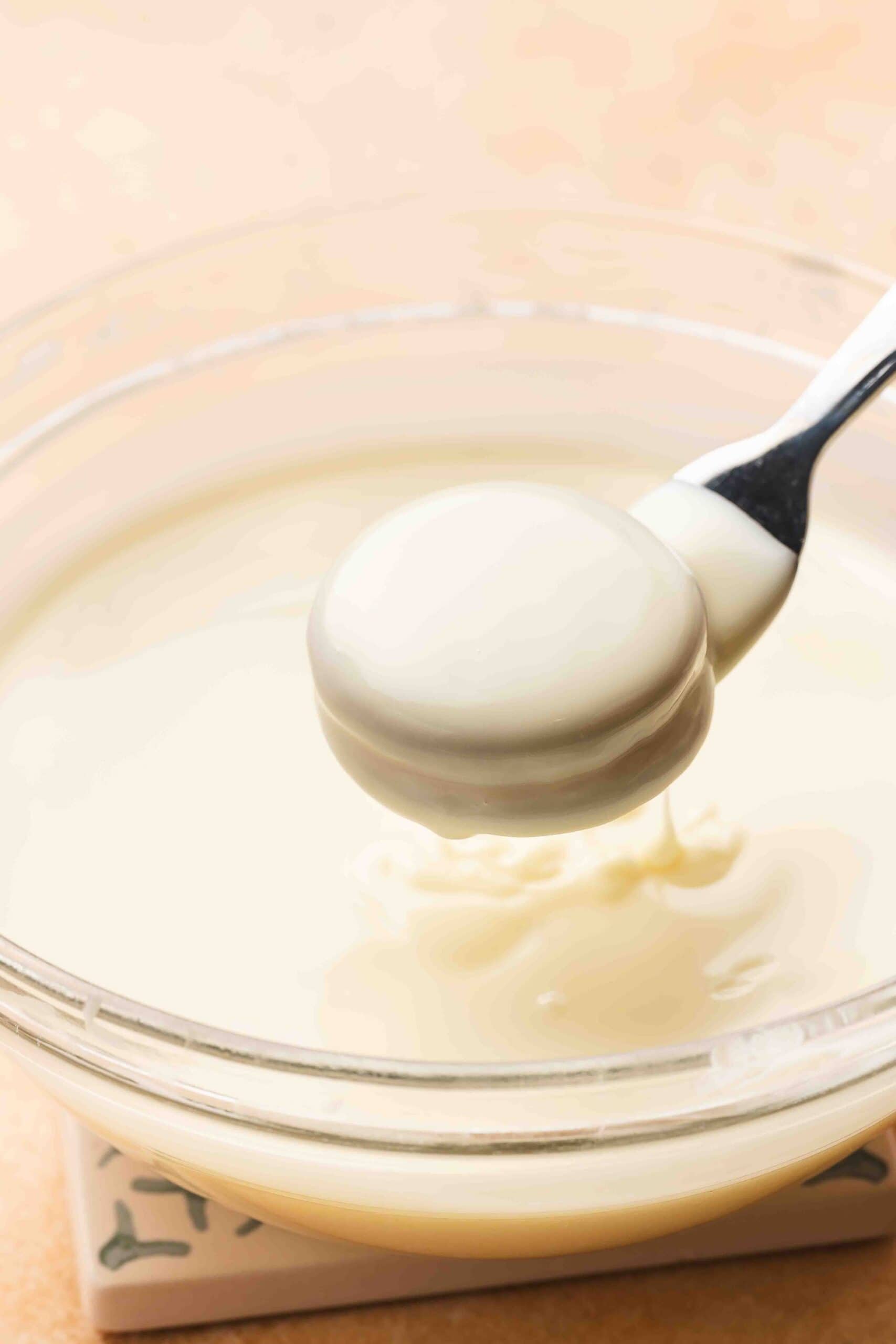 Dipping an Oreo into melted white chocolate using a fork and coating both sides evenly.