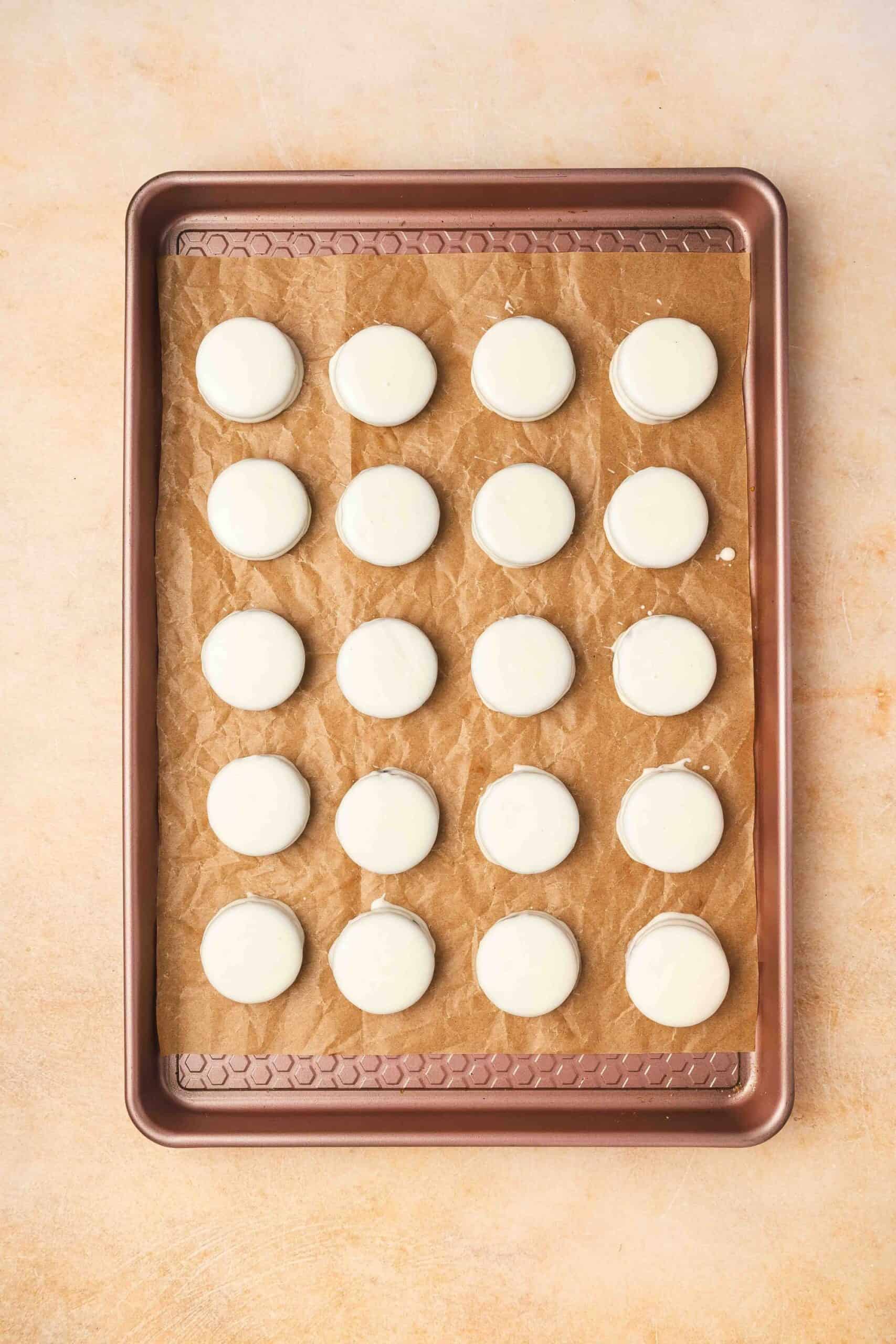 White chocolate covered Oreos placed on a parchment-lined tray and chilled to set.
