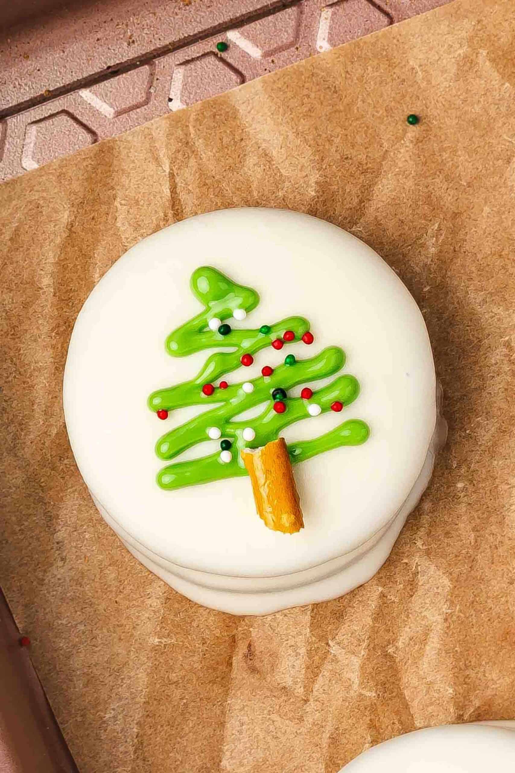 Decorating Oreos with pretzel trunks, Christmas sprinkles, and edible glitter while green drizzle is wet.