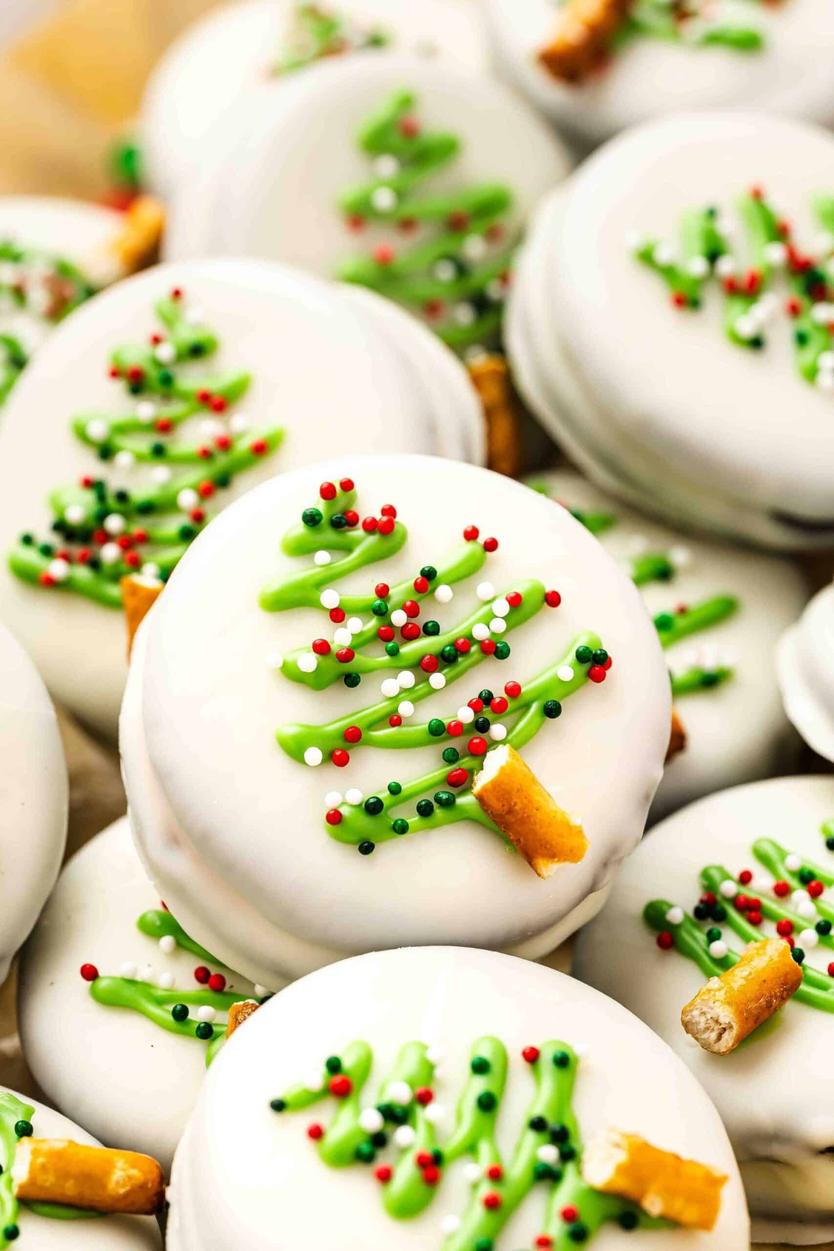 Close-up of a white chocolate covered Oreo showing the red filling inside, with festive sprinkles and green drizzle in the background.
