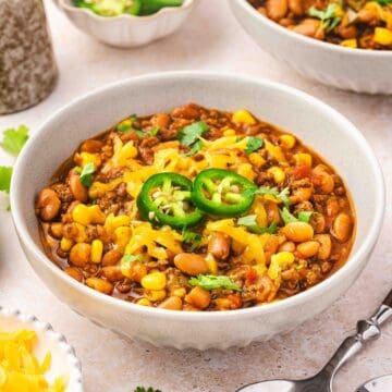 Hearty slow cooker beef and pinto bean chili served in a white bowl topped with cheddar, jalapeno, and cilantro.